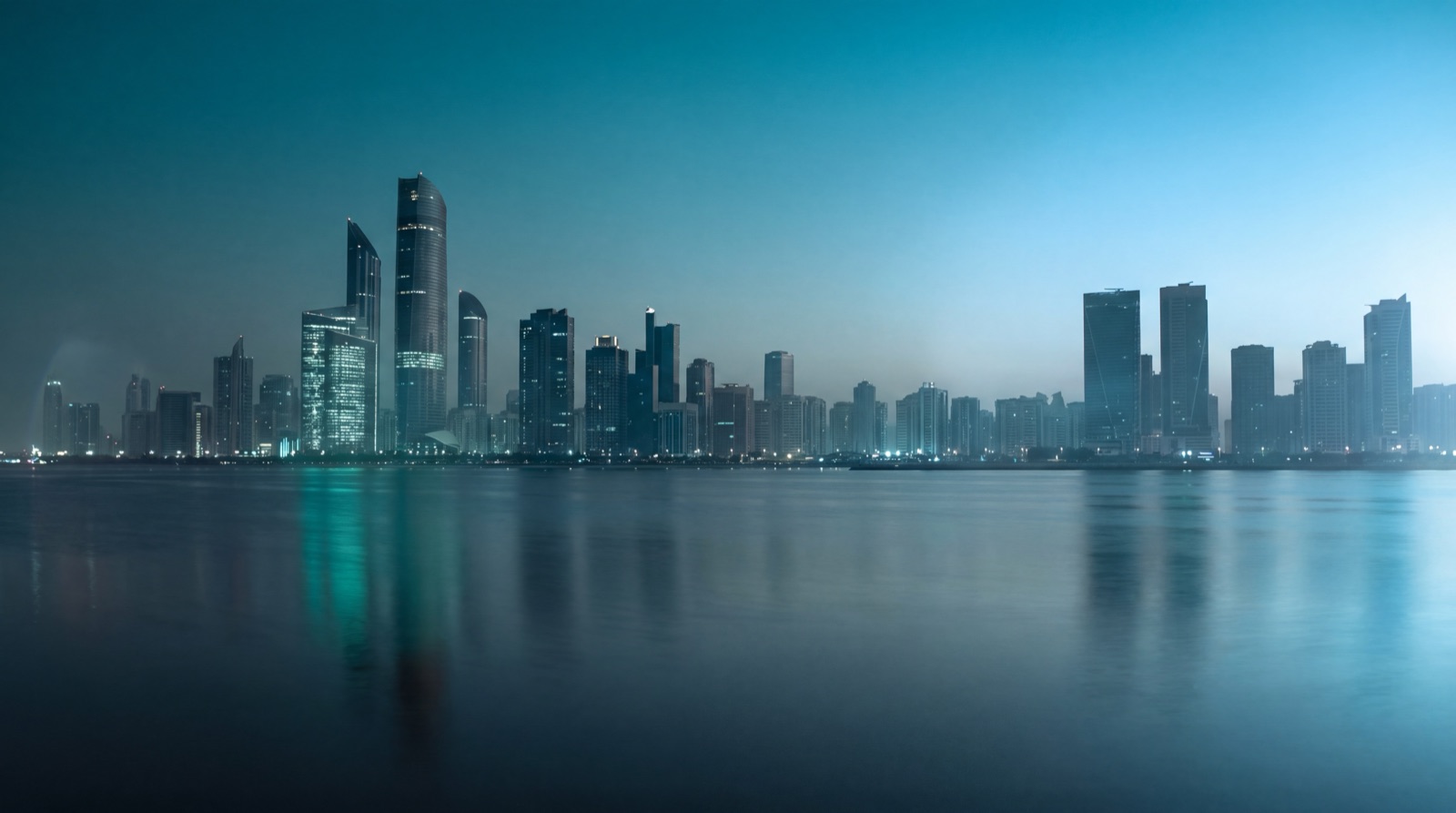 A Gulf city skyline at blue hour seen across calm water